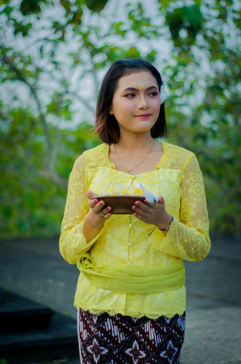 Portrait of young woman holding yellow while standing outdoors