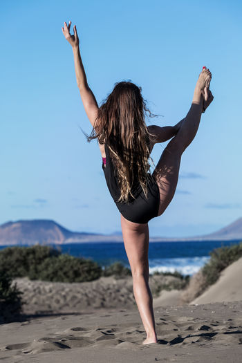 Full length of woman practicing yoga at beach against sky