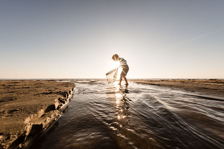 Young child walking in water with a net on a sunny morning at a beach