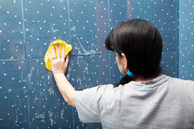 Woman wiping tiled wall at home