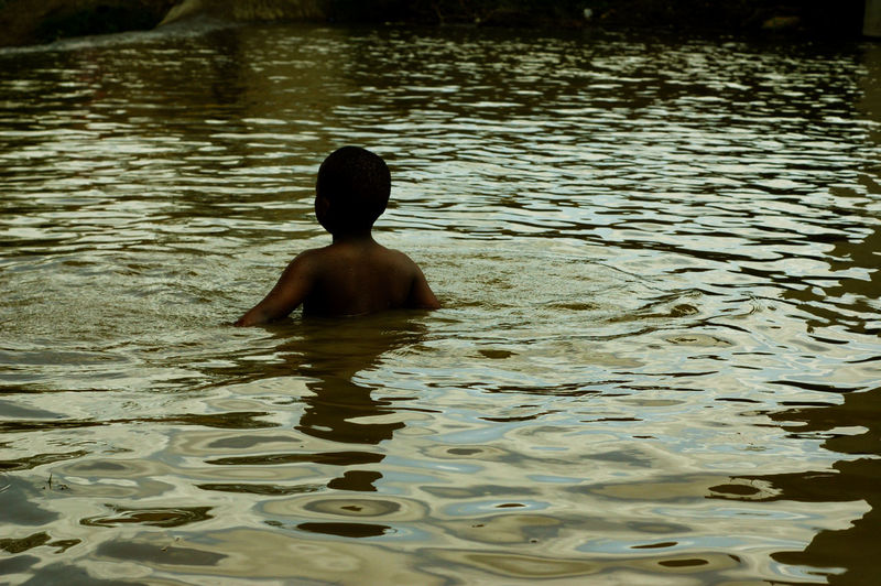 Rear view of shirtless boy swimming in water
