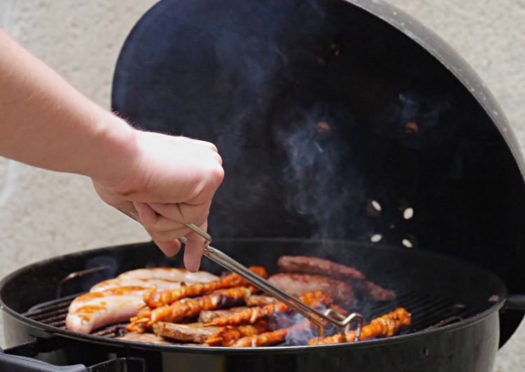 Cropped hand of man cooking meat on barbeque grill