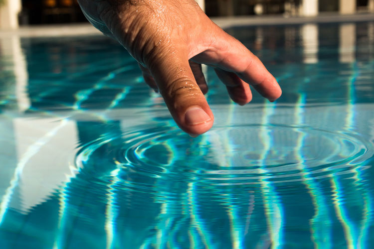 Cropped image of hand reaching at rippled water in swimming pool