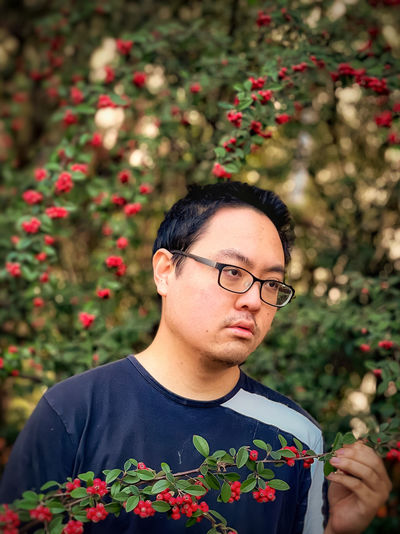 Portrait of young man holding rowan berry branch against rowan trees in woods.