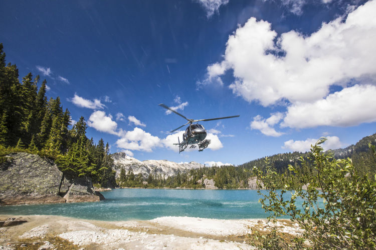 Helicopter in mid-air above alpine lake.
