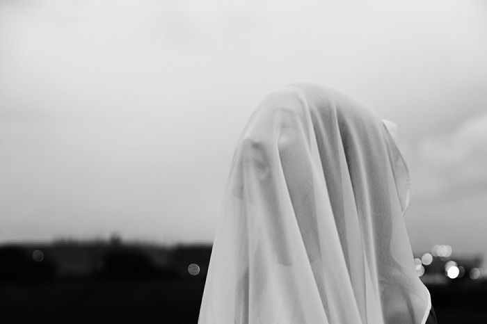 Close-up of woman covering face with fabric against sky