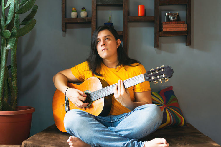 Man with long hair playing guitar at home in chill place pandemic time