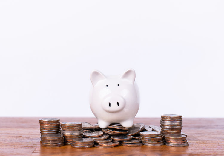 Close-up of coins and piggy bank against white background