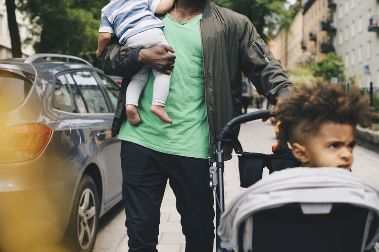 Father walking with children by baby stroller in city