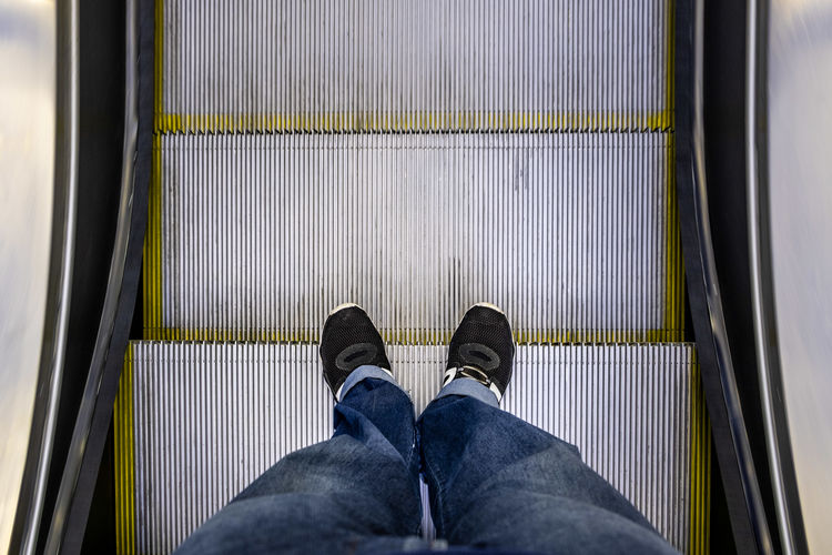 Male feet in jeans and black sneakers standing on escalator pov