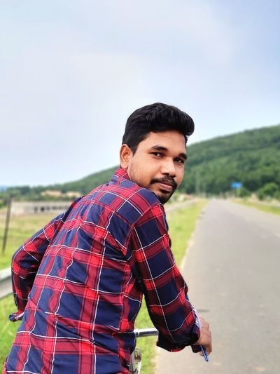 An indian young man riding bicycle and looking backwards for some reason. 