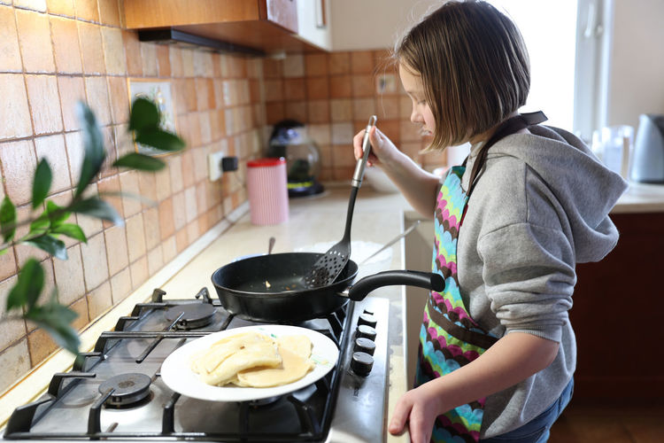 A girl cooks pancakes in the kitchen