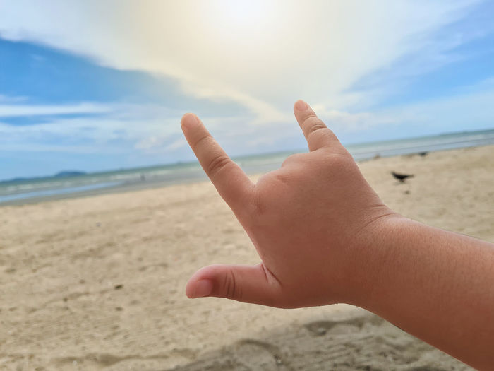 Cropped image of hand on sand at beach against sky