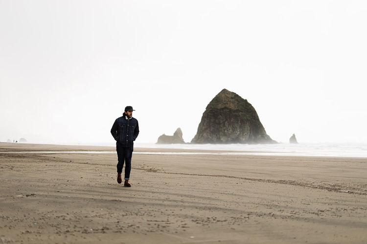Man traveler walking along foamy beach near sea on overcast day