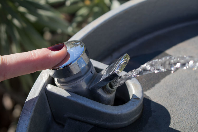 Close-up of woman pressing faucet of drinking fountain