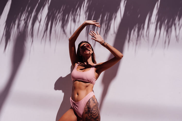 Young woman wearing bikini standing against wall