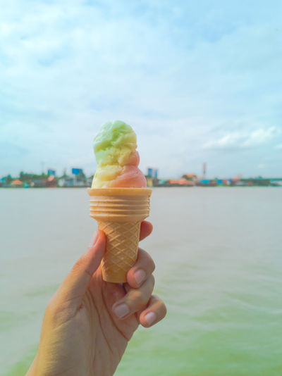 Cropped image of hand holding ice cream cone against sky