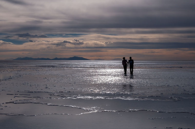 Silhouette men on beach against sky during sunset