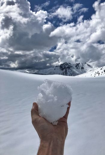 Person holding umbrella on snowcapped mountain against sky