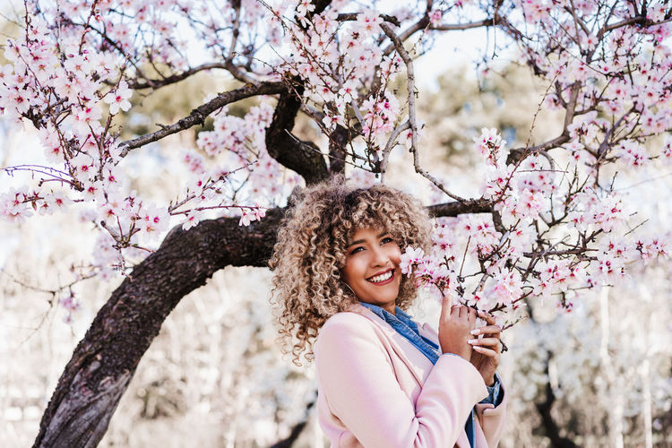 Portrait of beautiful hispanic woman with afro hair in spring among pink blossom flowers. nature