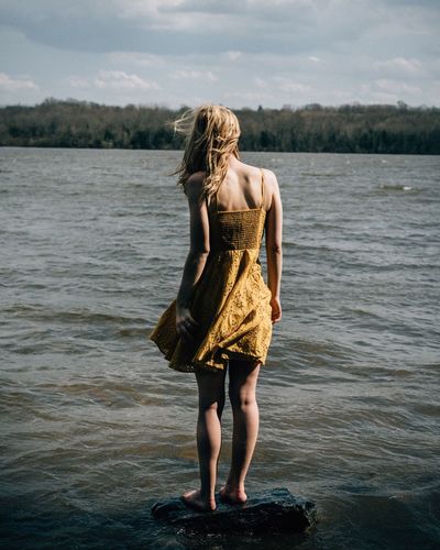 Rear view of young woman standing in sea against sky