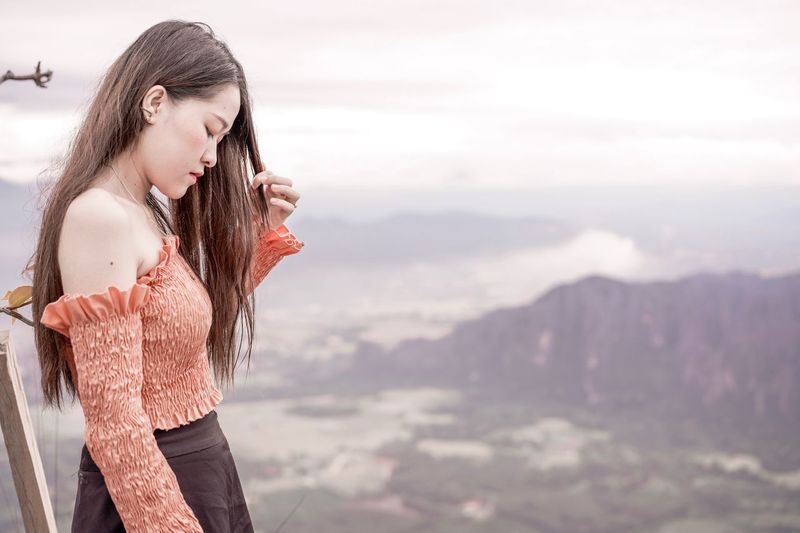 Beautiful young woman standing on mountain against sky