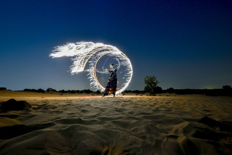 Full length of woman standig on sand against wire wool and sky
