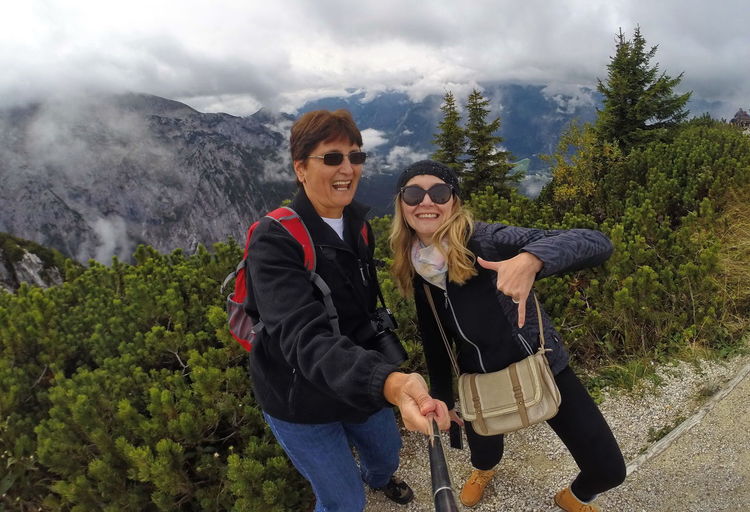 Portrait of cheerful female friends standing on mountain against cloudy sky