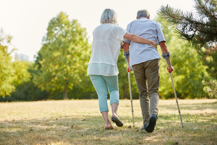 Rear view of woman assisting man walking with canes