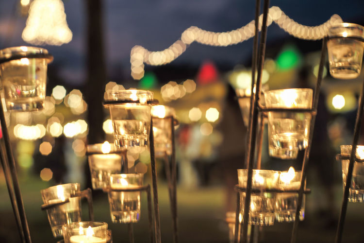 Close-up candle in small glass jars in the steel holder with blurred bokeh lights background