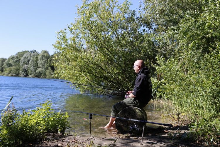 Man fishing in lake against trees