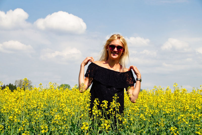 Portrait of smiling young woman standing on oilseed rape field