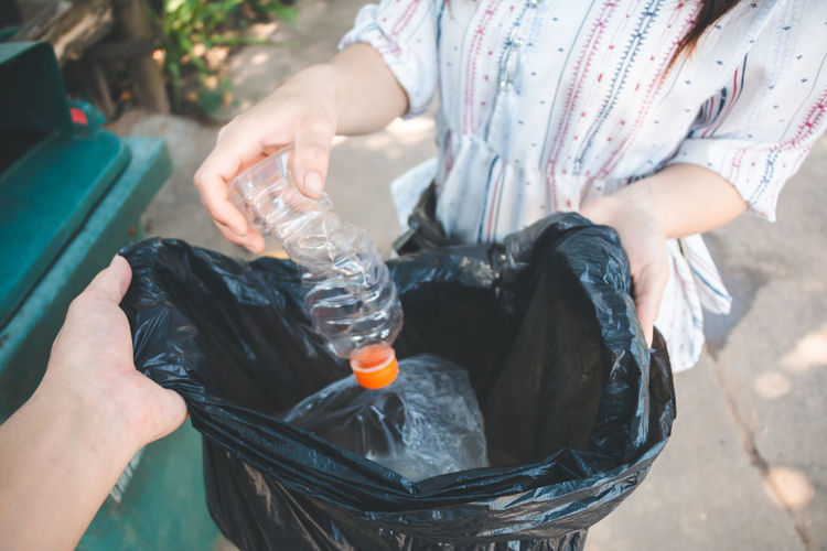 Midsection of woman putting plastic bottle in bag