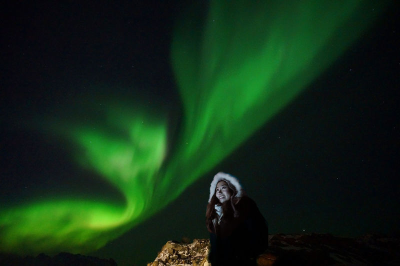 Low angle view of woman standing against aurora borealis at night
