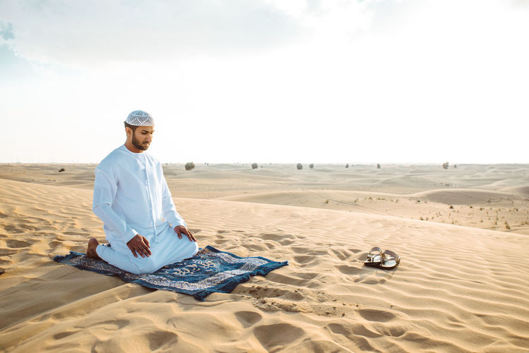 Man praying while sitting on sand in desert