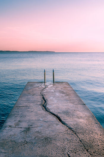 View over the sea during sunset on a dock with a crack leading the viewers eye into the water.