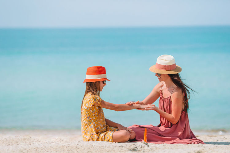 Mother applying suntan lotion on beach to daughter