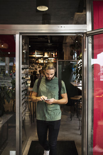 Full length of man using mobile phone while walking at restaurant doorway