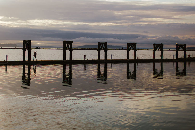 Wooden posts in sea against sky during sunset