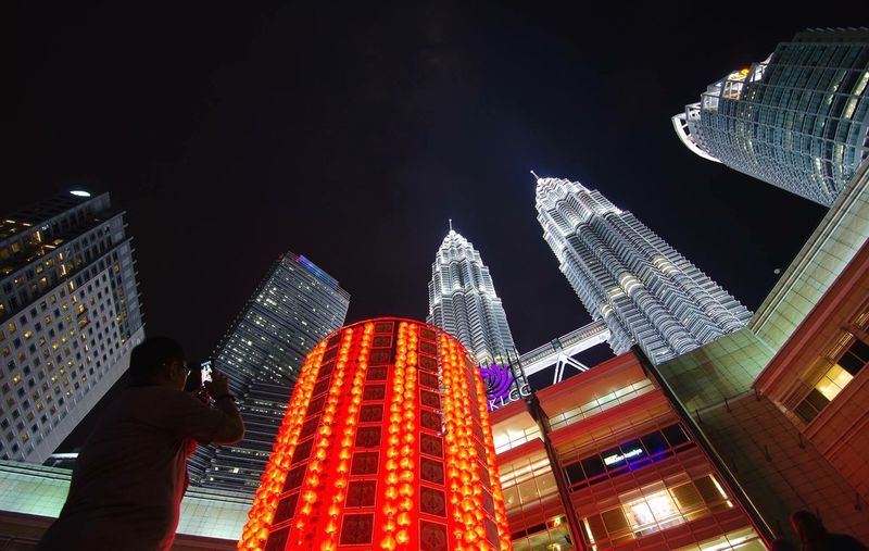 Low angle view of man photographing illuminated petronas towers against sky at night