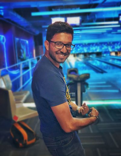 Portrait of smiling young man posing while standing against bowling alley