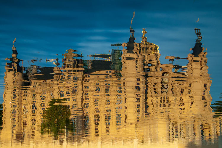 Reflection of built structure castle in water against blue sky