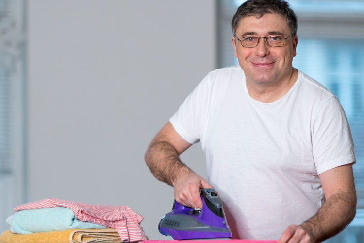 Portrait of smiling man ironing cloth at home