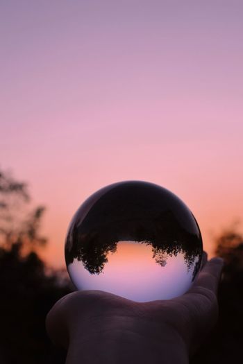 Silhouette person holding crystal ball against sky during sunset