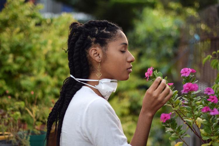 Young woman takes face mask off to smell the flowers