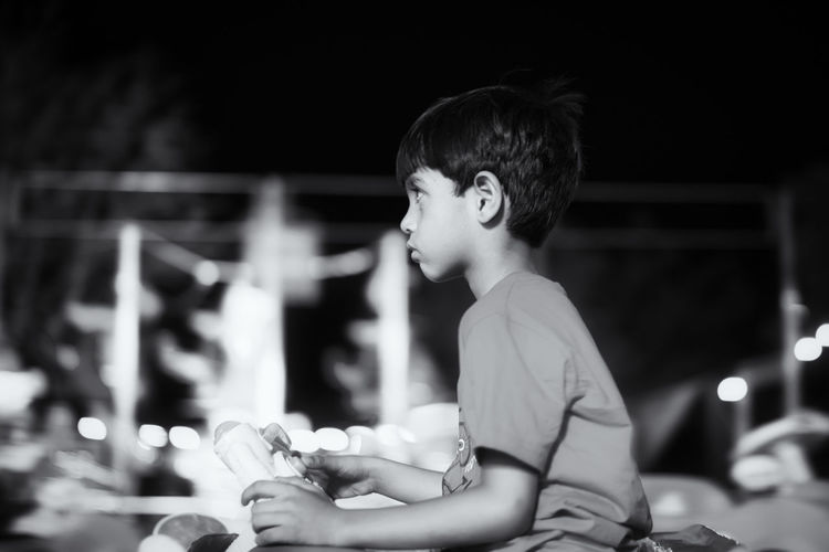 Side view of thoughtful boy sitting against sky at night