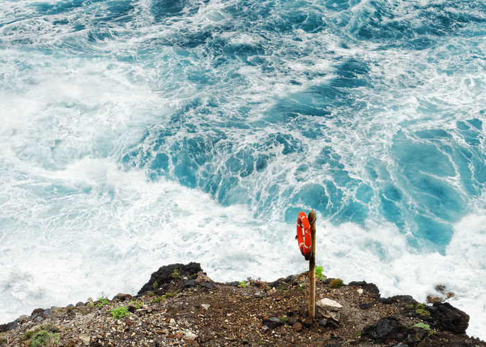 On a steep rocky coast view from above on a red lifebuoy in front of a dangerous wild surf