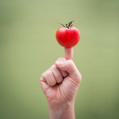 Close-up of finger with tomato against green background