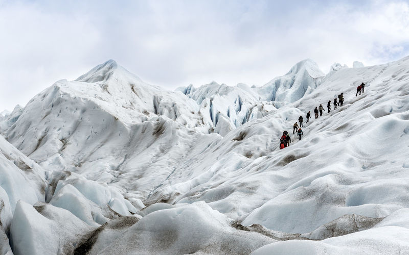 Low angle view of people climbing on glacier against sky