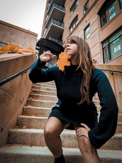 Low angle view of woman holding maple leaf while standing on steps during autumn